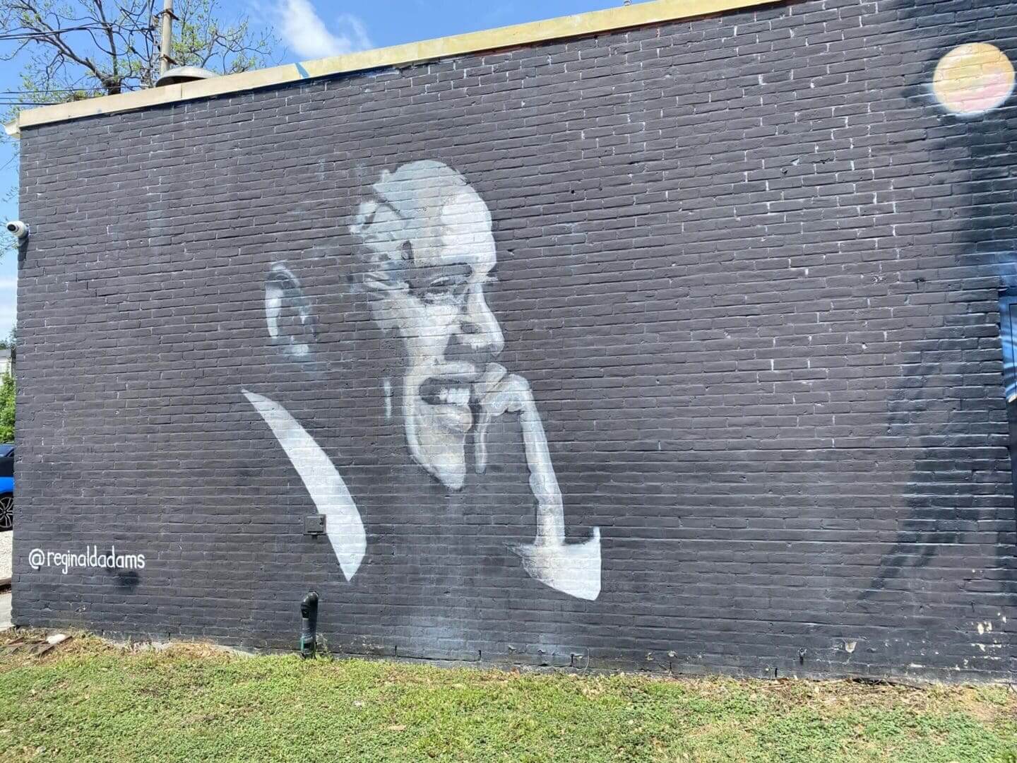 Black and white mural of an elderly man smiling on a brick wall.