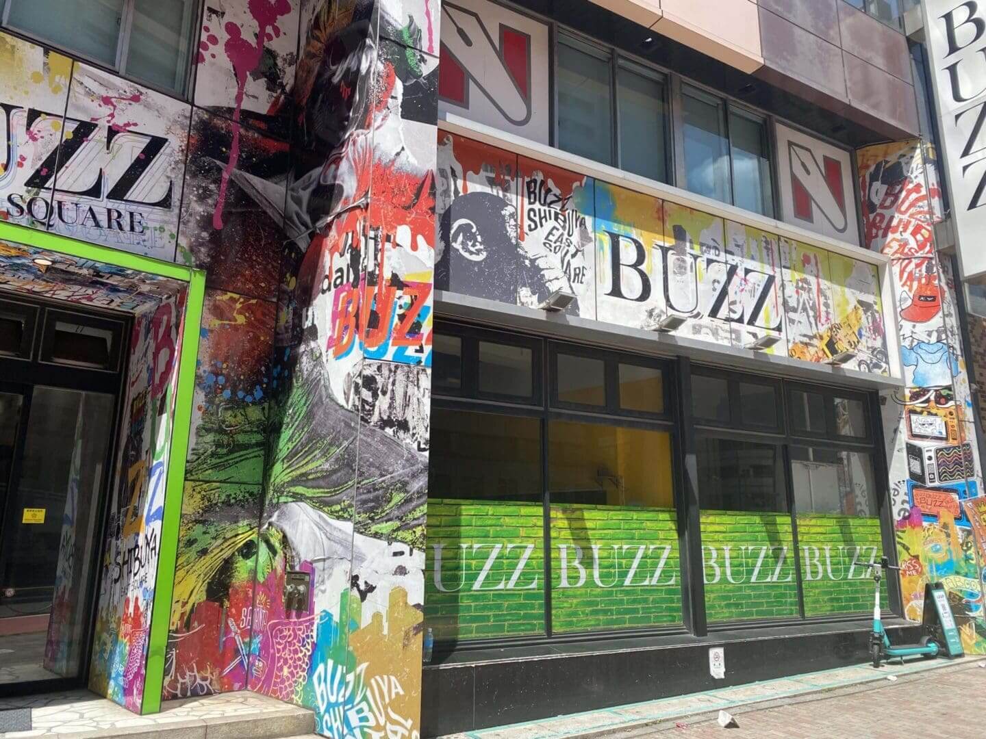 Colorful graffiti and posters cover a building facade and a column.