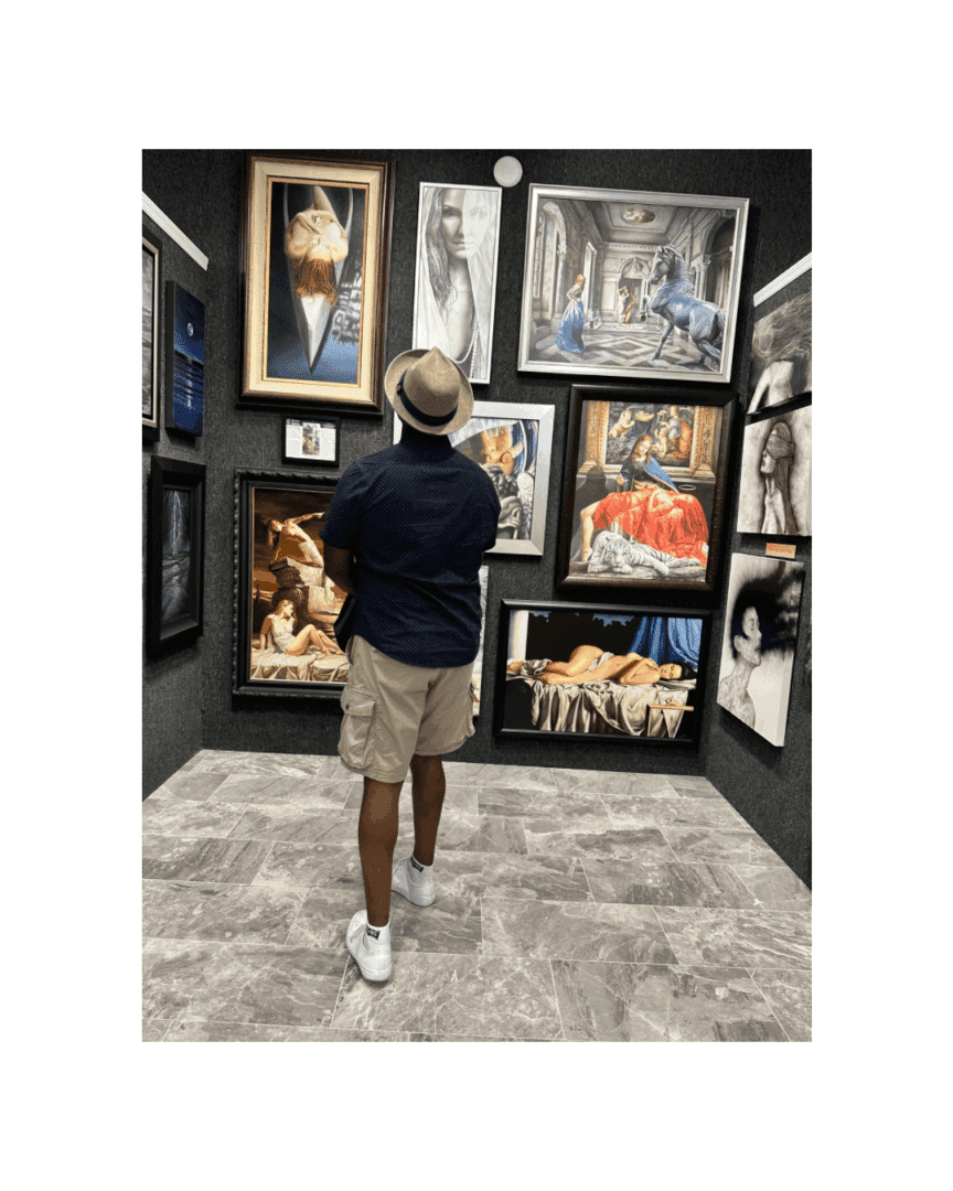 A man in a hat and shorts viewing artwork in a gallery.