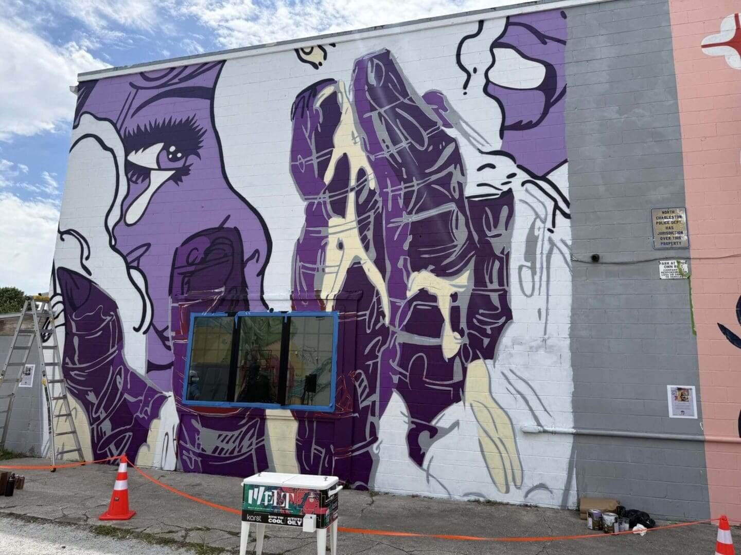 Large mural of purple praying hands on a gray wall with a window.