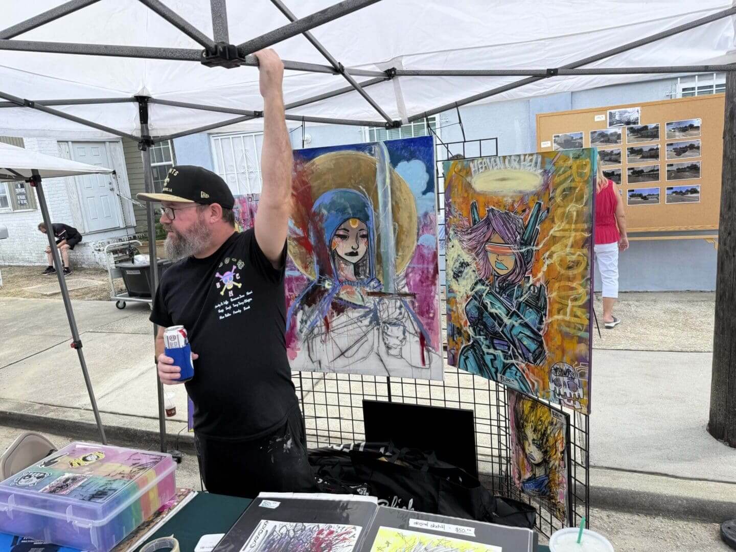 Artist showcasing vibrant paintings at an outdoor market tent.