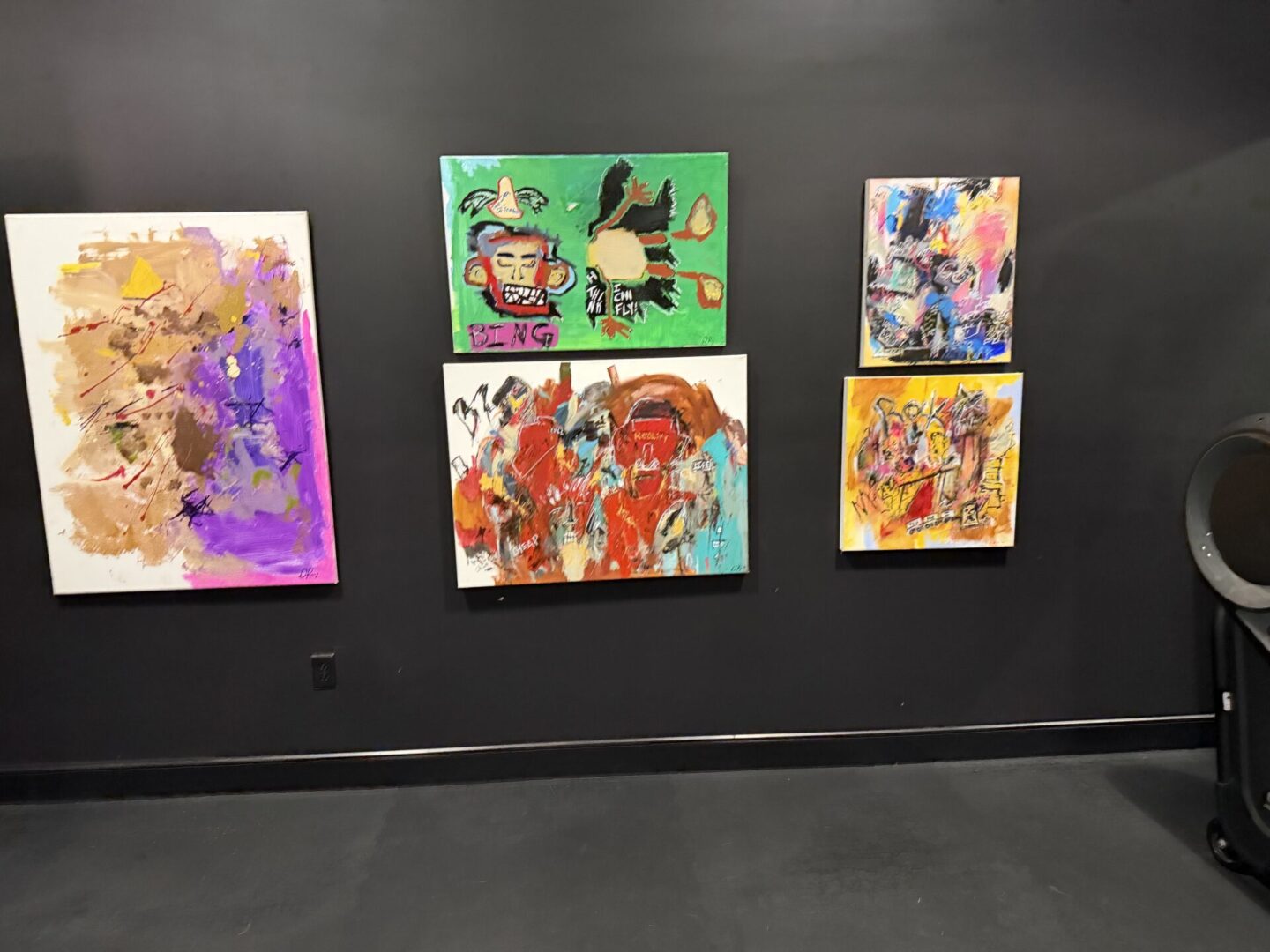 Colorful abstract paintings on a black wall.